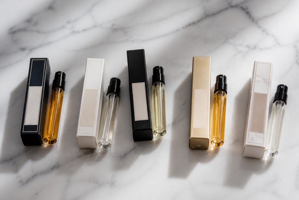 Five elegant glass fragrance sample vials and boxes arranged on a marble surface in soft natural light