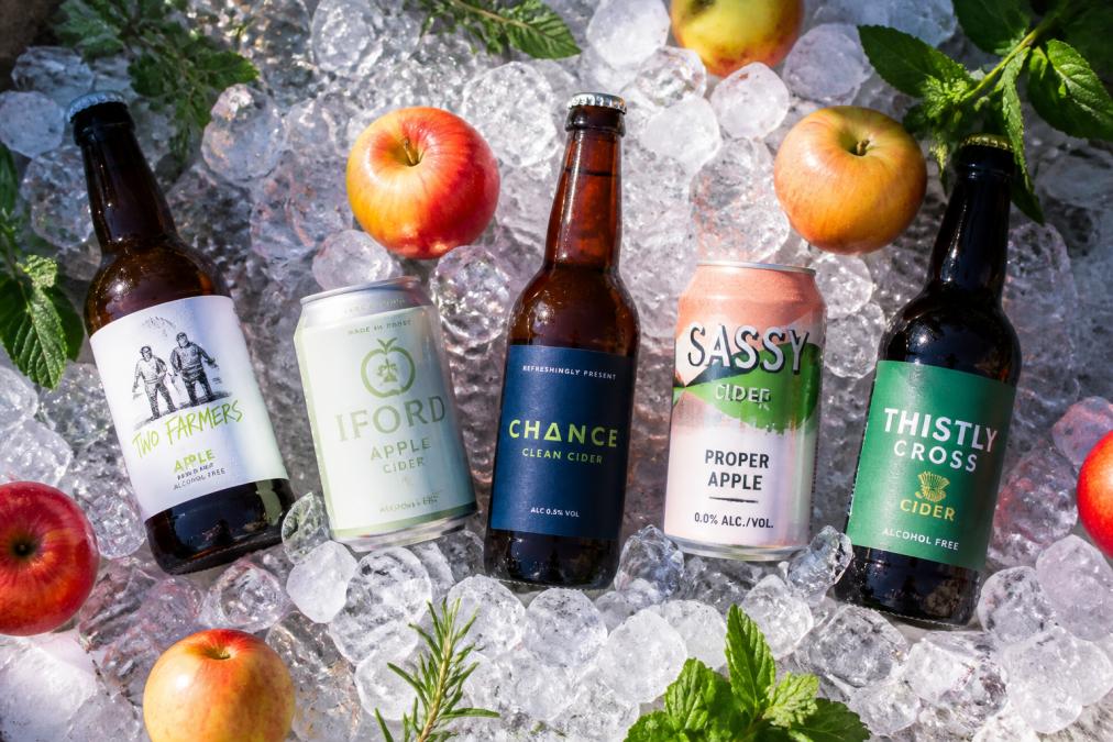 Five bottles and cans of the best non alcoholic cider for summer chilled on ice with fresh apples and green herbs