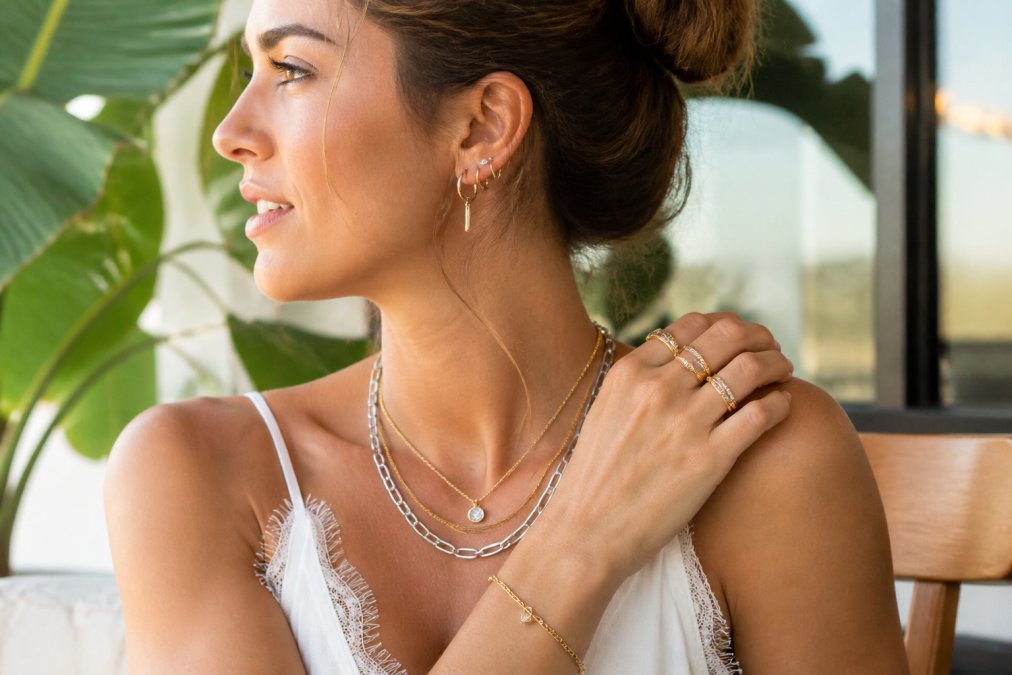 Woman wearing a curated mix of sterling silver and gold-filled jewelry pieces layered together in natural daylight, showcasing the shine and fine detail of delicate rings, earrings, and layered necklaces