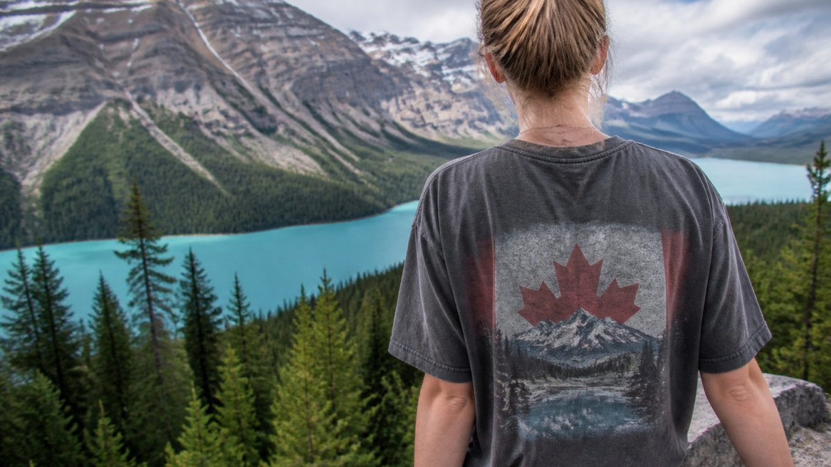 Personne portant un t-shirt teint en pièce sur le thème canadien, en extérieur avec un paysage de montagnes en arrière-plan, montrant la texture vintage et la coupe décontractée du vêtement