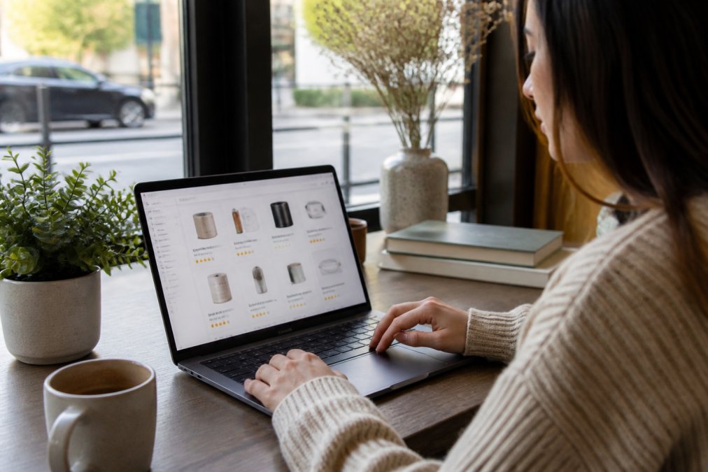 Person browsing on a laptop with a cup of coffee nearby, examining product details and reading reviews on a curated shopping website with natural window lighting