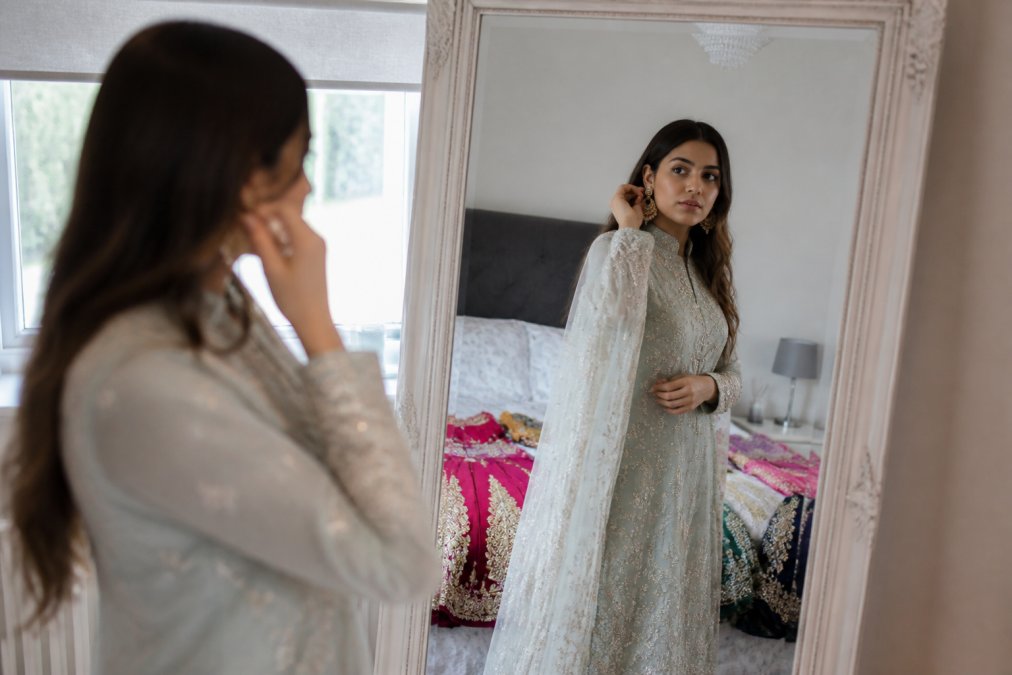 A woman trying on an embellished Pakistani salwar kameez found at the best online stores for Eid in her bedroom.