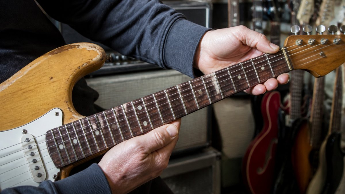 Close-up of hands carefully examining a vintage electric guitar's fretboard, neck joint, and tuning machines in natural light, checking for wear and damage