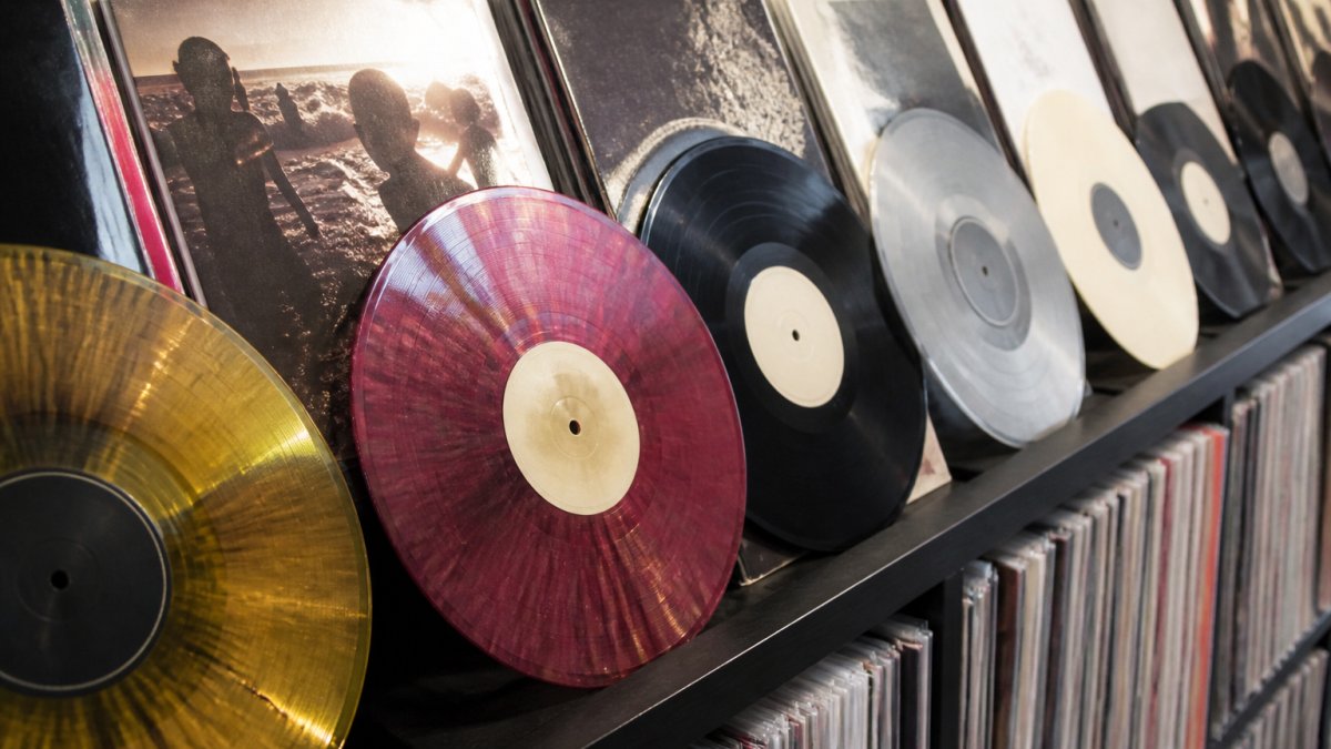 Close-up of vinyl records arranged on a shelf, showing coloured pressings and album artwork detail, with natural lighting highlighting the record grooves and labels