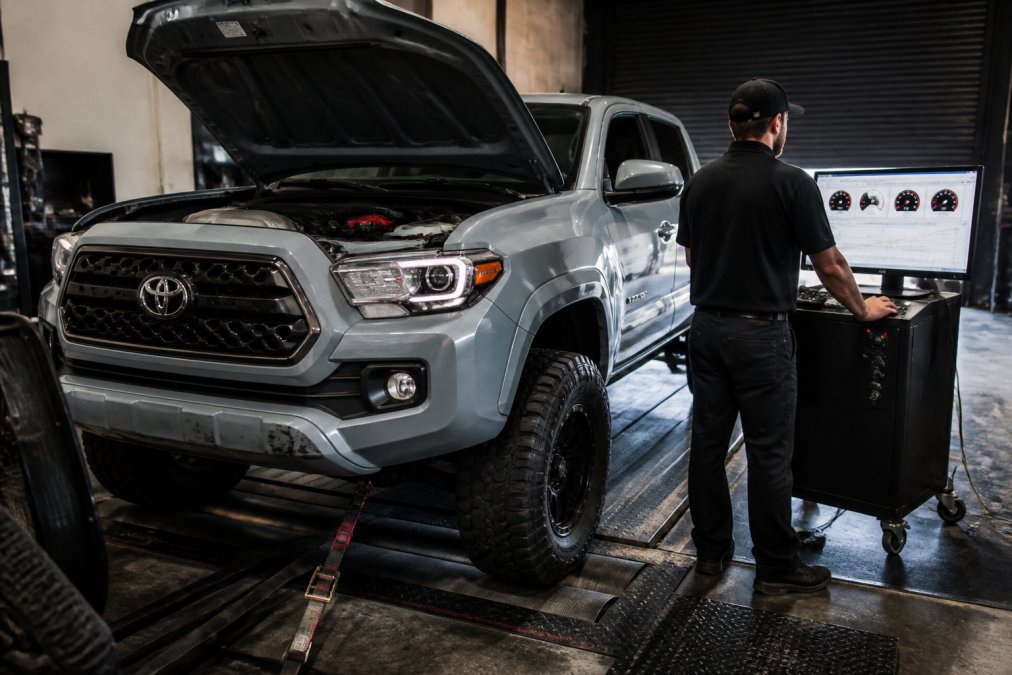 Toyota Tacoma positioned on a dynamometer during performance testing, with a technician in professional attire monitoring power output readings and performance metrics on the dyno control screen in a well-equipped testing facility