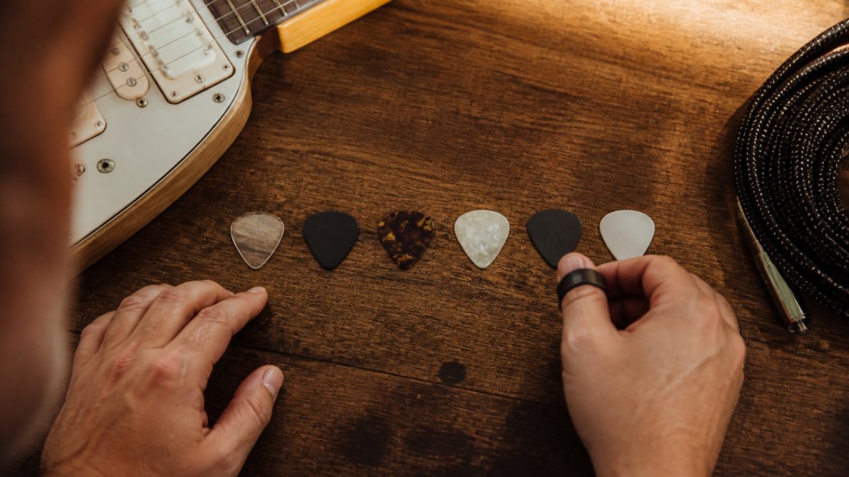 Six electric guitar picks arranged on wood, labeled by pick thickness in millimeters next to a guitar body.