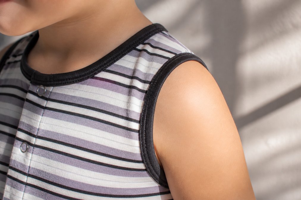 Close-up of a child's shoulder wearing soft bamboo fabric, showing the tagless seam detail and smooth texture against sensitive skin, natural sunlight creating gentle shadows on the fabric