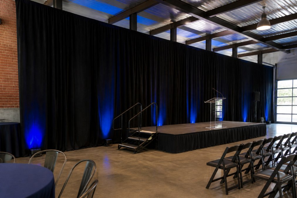 Professional event setup with elegant black velour drapes framing a corporate stage, showing properly installed uprights, crossbars, and base plates with subtle event lighting in modern venue