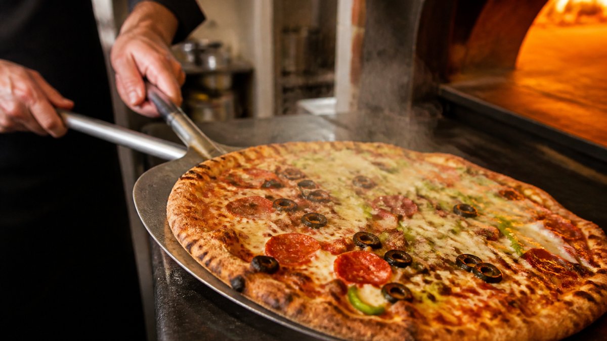 A fresh, hot hand-tossed pizza with melted cheese and toppings just pulled from the oven, steam rising in a modern kitchen with warm lighting