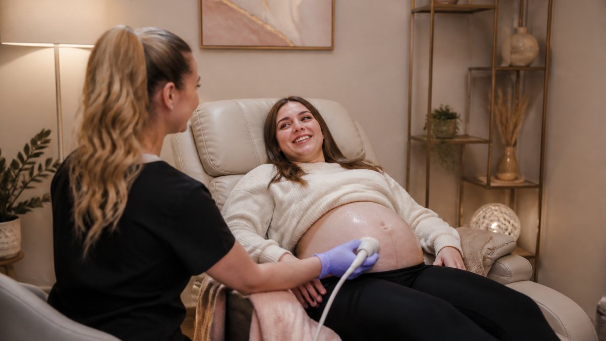 Expectant mother in comfortable reclining chair receiving 3D ultrasound scan from trained technician in modern, softly lit studio with warm neutral tones and calming decor