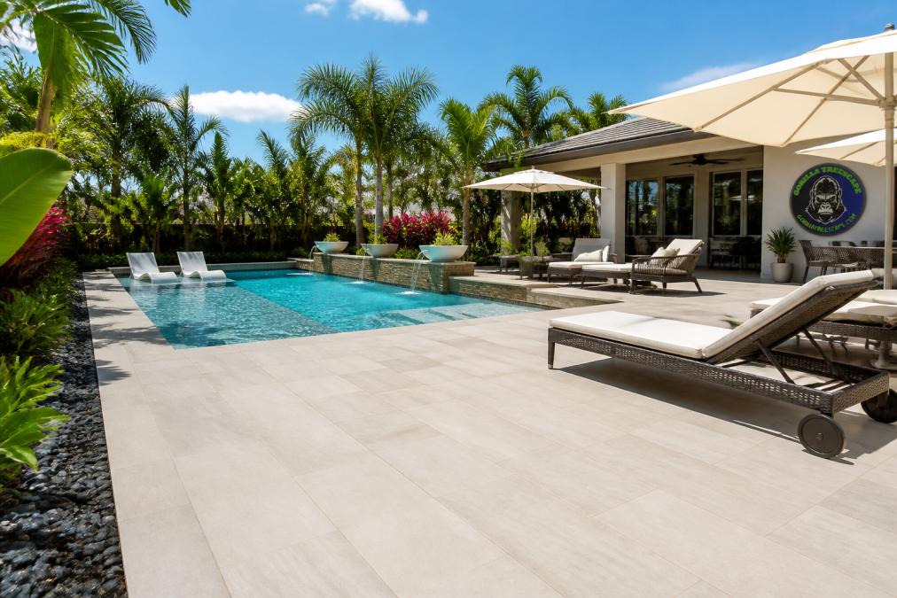 Large-format porcelain pool patio paving surrounds a backyard pool with lounge chairs and tropical landscaping.