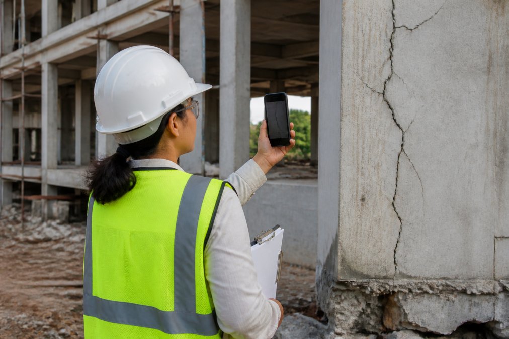 Inspector in high-visibility gear using a smartphone for field documentation of a construction site defect.