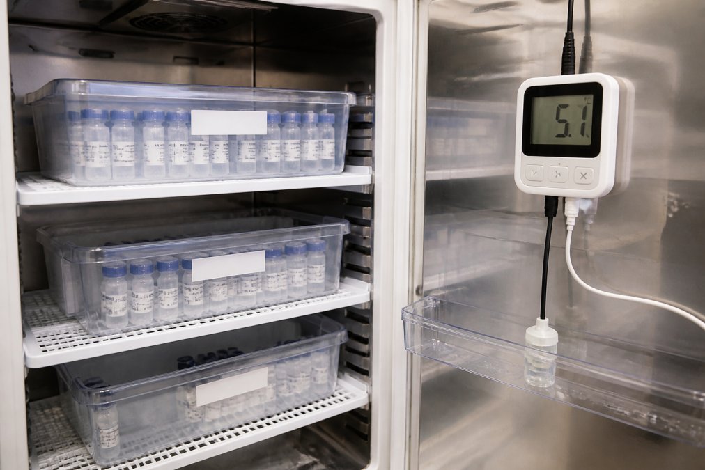 Peptide vials stored in a refrigerated unit with temperature monitoring equipment visible, showing organized storage with labeled containers and thermometer display