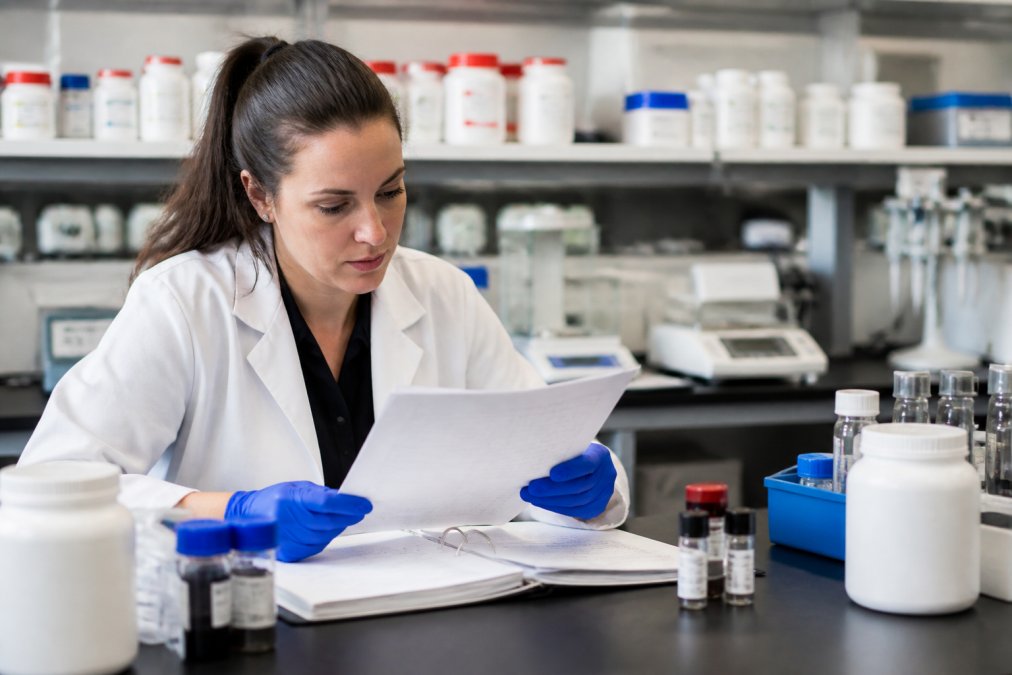 Researcher or lab technician examining peptide documentation and certificates of analysis at a workspace with laboratory equipment in background, reviewing quality records and batch information