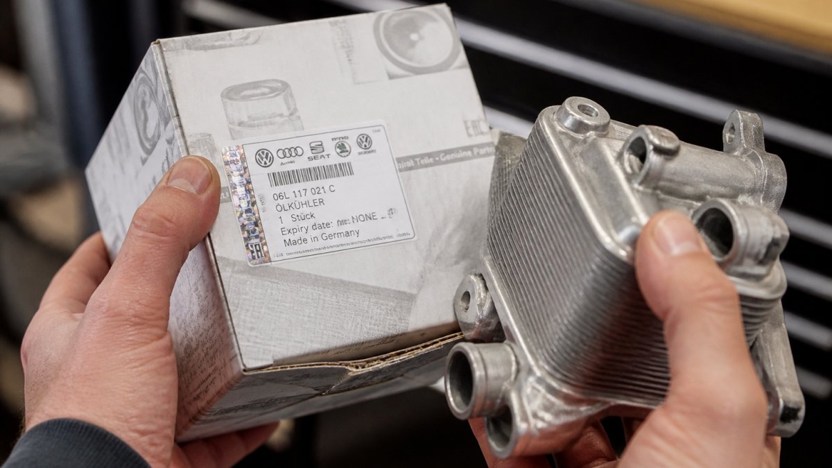 Close-up of hands examining an Audi OEM part number label and packaging, showing authentic hologram or security features on a genuine part