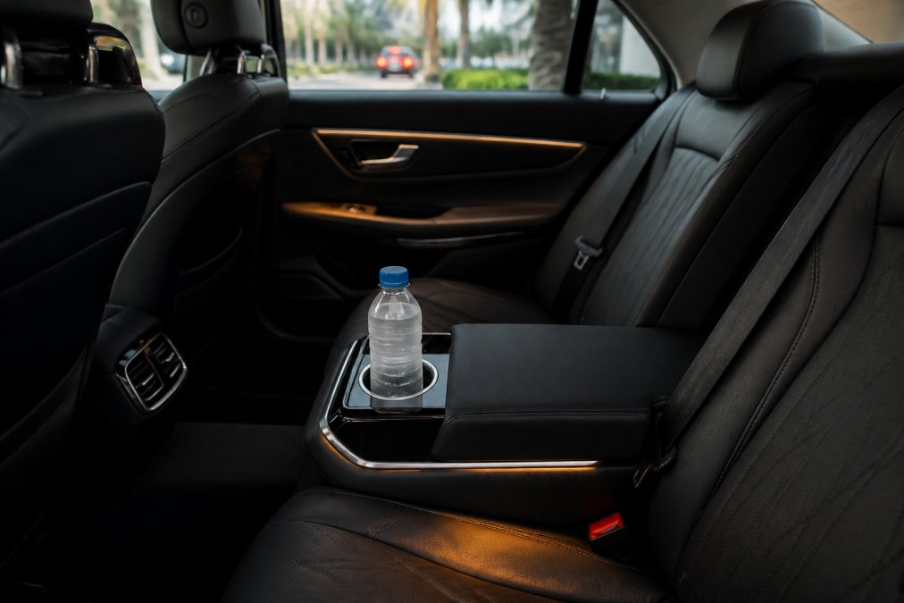 Interior of a luxury executive sedan showing immaculate dark leather seats, a chilled water bottle in the illuminated armrest console, and soft ambient cabin lighting in a pristine, uncluttered interior