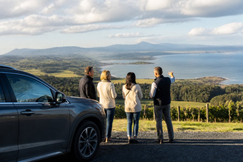 A local guide and travellers with private tour guides overlooking a Tasmanian coastal landscape at sunset.
