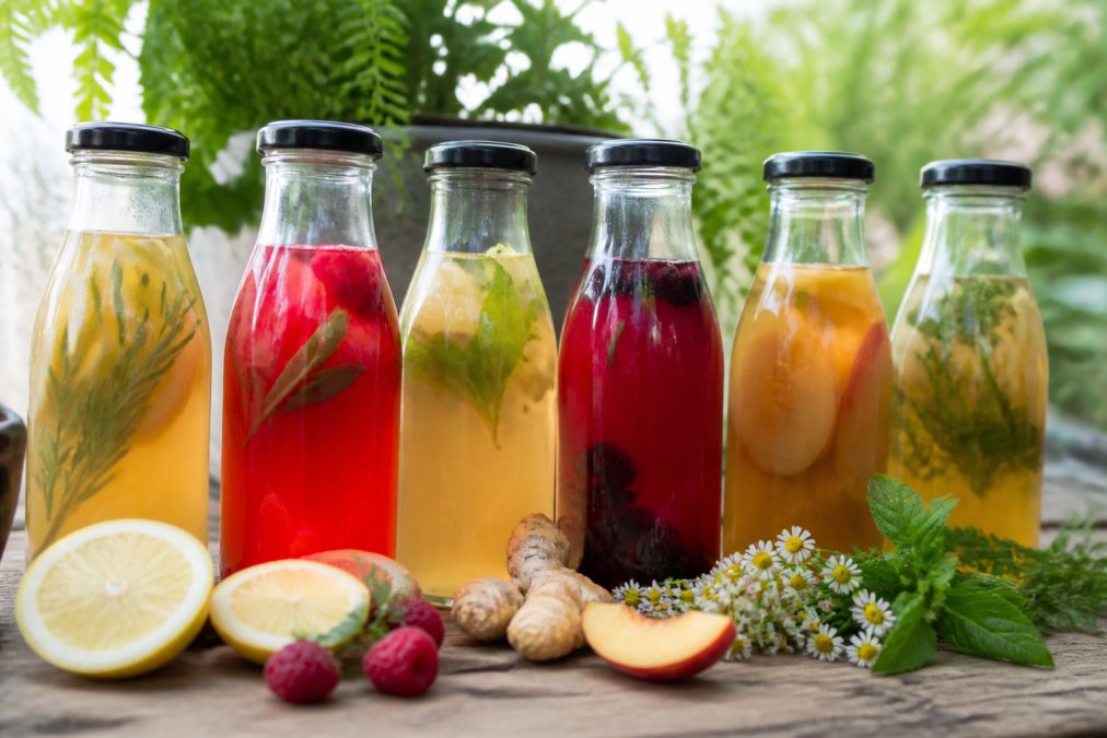 Close-up of colorful fermented beverages in glass bottles with fresh fruit and botanicals visible, emphasizing natural ingredients and vibrant presentation