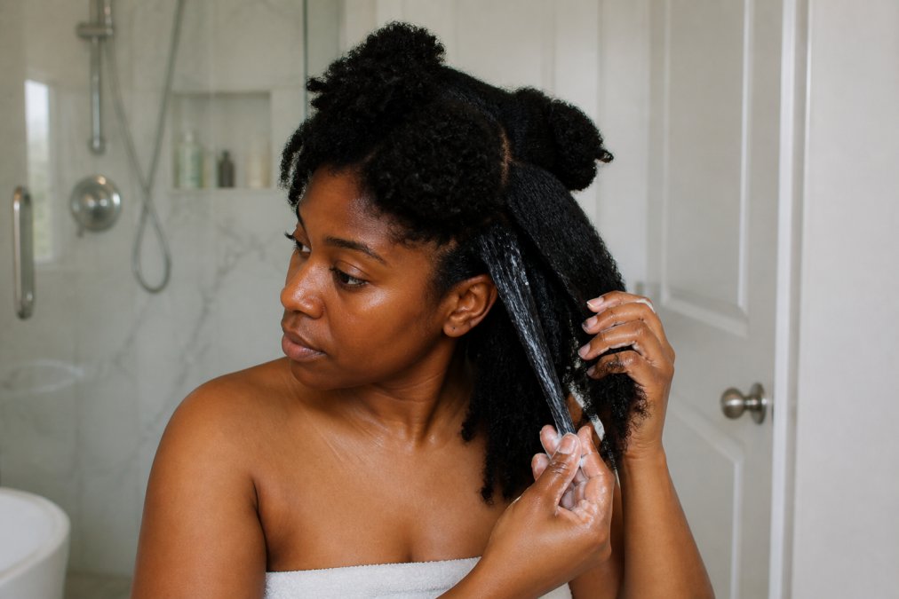 Black woman applying best products for 4b hair as leave-in conditioner to her coily hair in sections