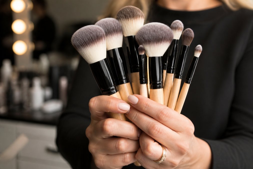 Makeup artist holding professional makeup brush sets with soft studio lighting on the synthetic bristles and wooden handles.