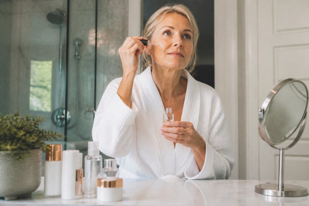 Woman in her 50s applying professional skincare for mature skin serum in a bright, modern bathroom setting