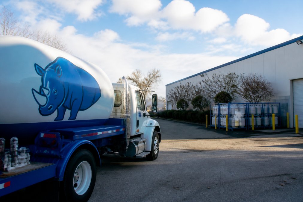 Propane delivery truck with Blue Rhino branding arriving at a commercial facility parking lot during morning hours with clear skies