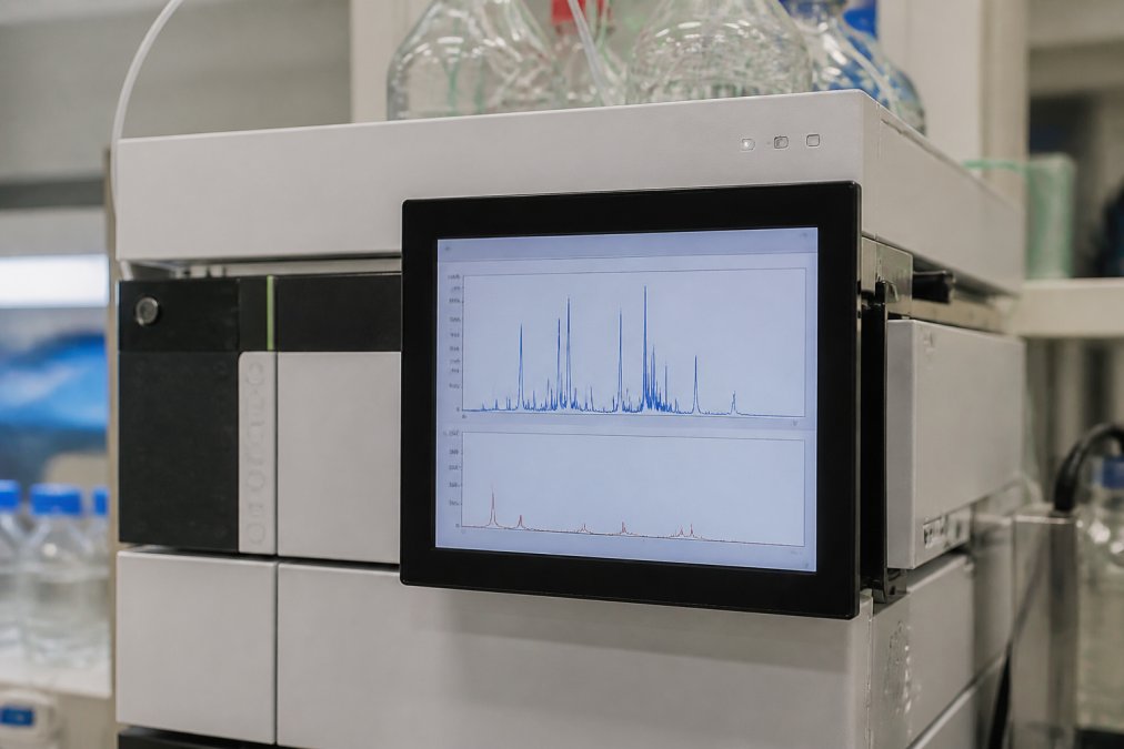 Close-up of a high-performance liquid chromatography instrument display screen showing analytical chromatogram peaks and data from peptide testing in a modern laboratory setting