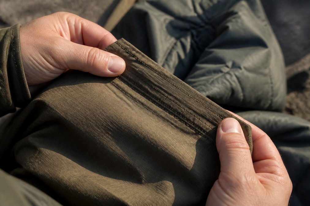 Close-up of outdoor apparel fabric being examined by hands, showing stitching details, seam construction, and weave pattern under natural lighting