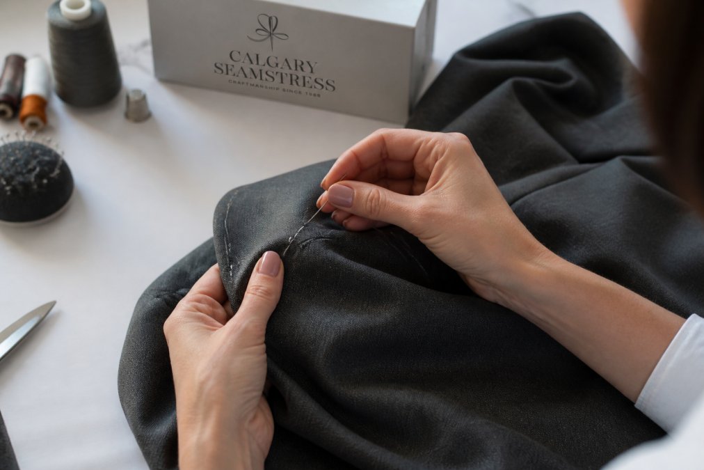 Close-up of seamstress's hands working on suit jacket seams with needle and thread, showing detailed stitching technique with natural lighting