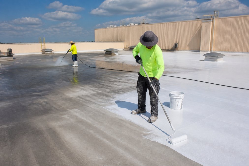 Worker pressure washing a roof and applying primer before reflective roof coatings are installed