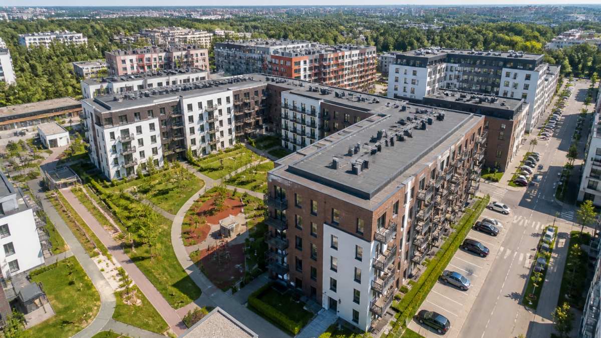 Aerial view of modern residential development with completed apartment buildings, manicured landscaping, paved roads, and common recreational areas in a thriving urban neighbourhood