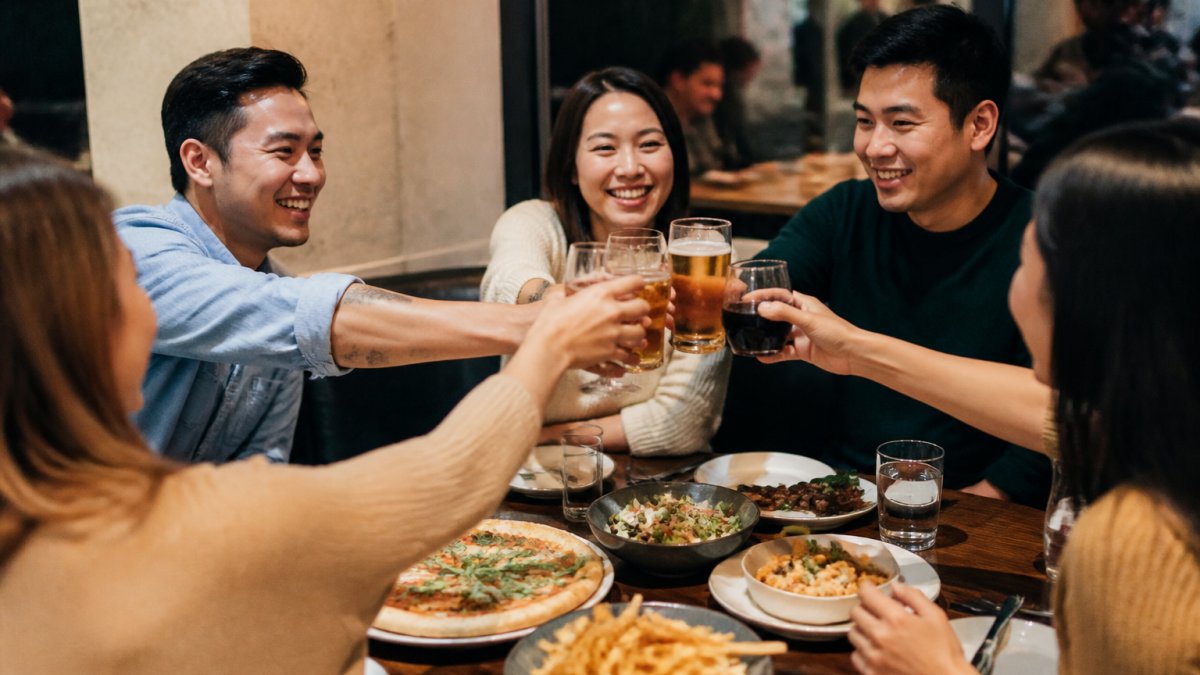 A group of friends enjoying a meal together at a casual restaurant, smiling and raising glasses in celebration, with food and drinks on the table