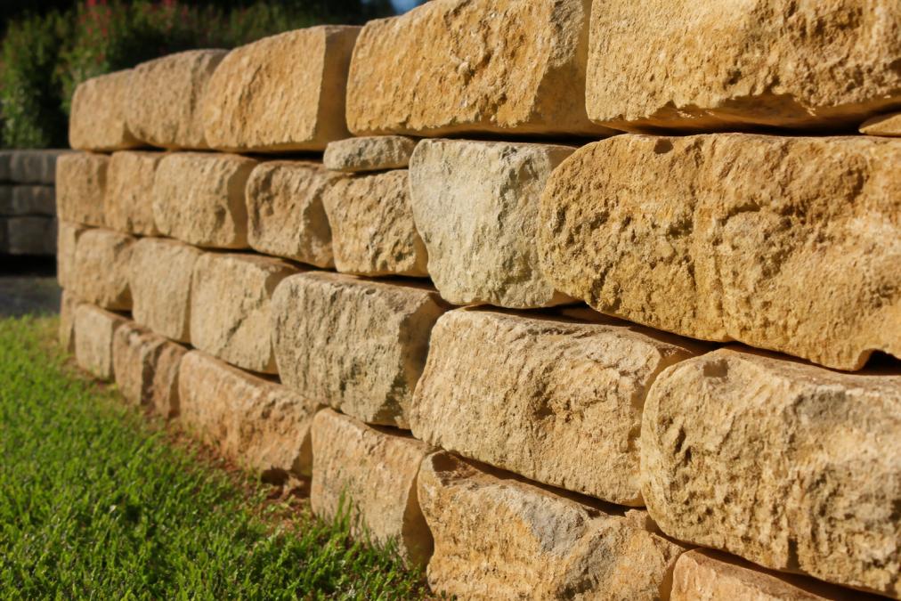 Close-up of stacked Lueders Buff natural stone retaining wall showing warm golden and cream-colored stone texture with natural face variations in bright afternoon sunlight, individual stones fitted tightly together