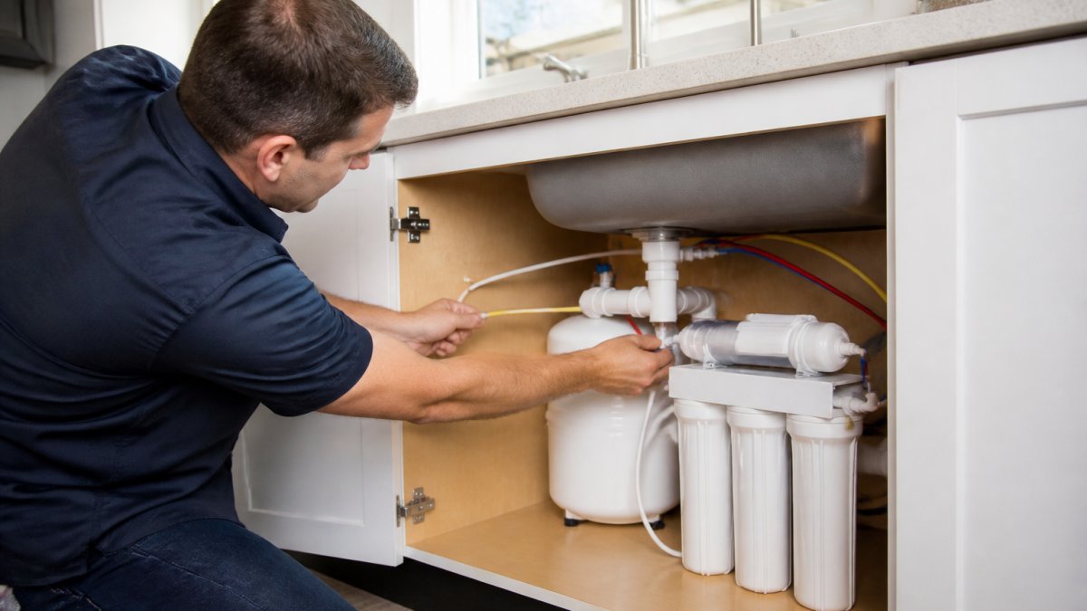Professional technician installing an under-sink reverse osmosis system using precision tools in a kitchen