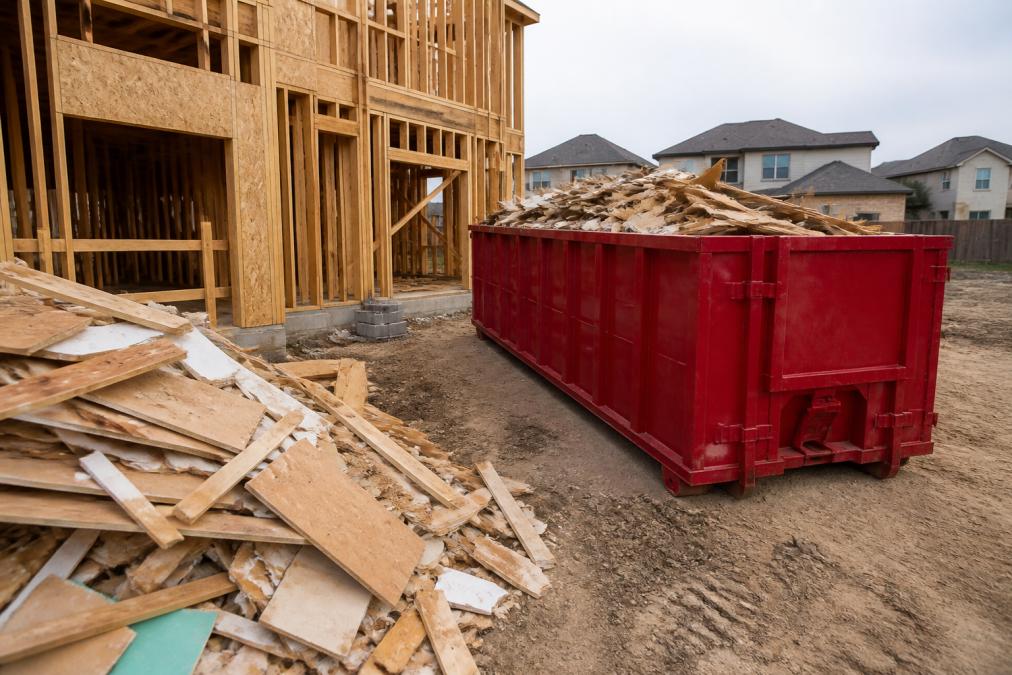 Construction site with a roll-off dumpster properly positioned near the work area, showing organized debris placement and clear access for loading materials
