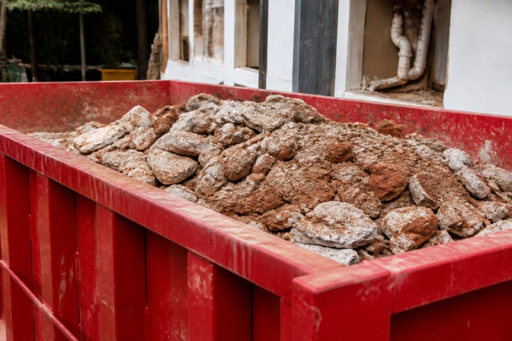 Close-up view of heavy construction materials like concrete chunks, bricks, and dirt piled in a 15-yard dumpster during a demolition or renovation project