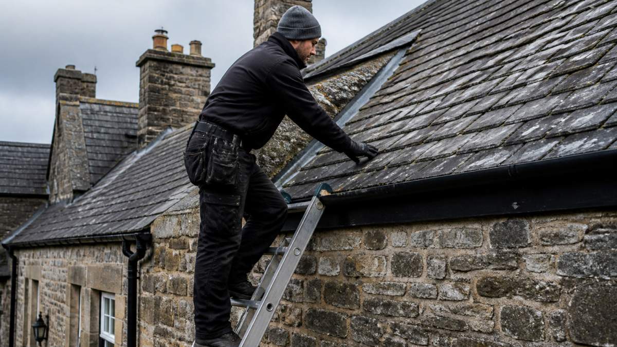 Roofer inspecting a slate roof on a stone house to determine if a roof replacement is needed
