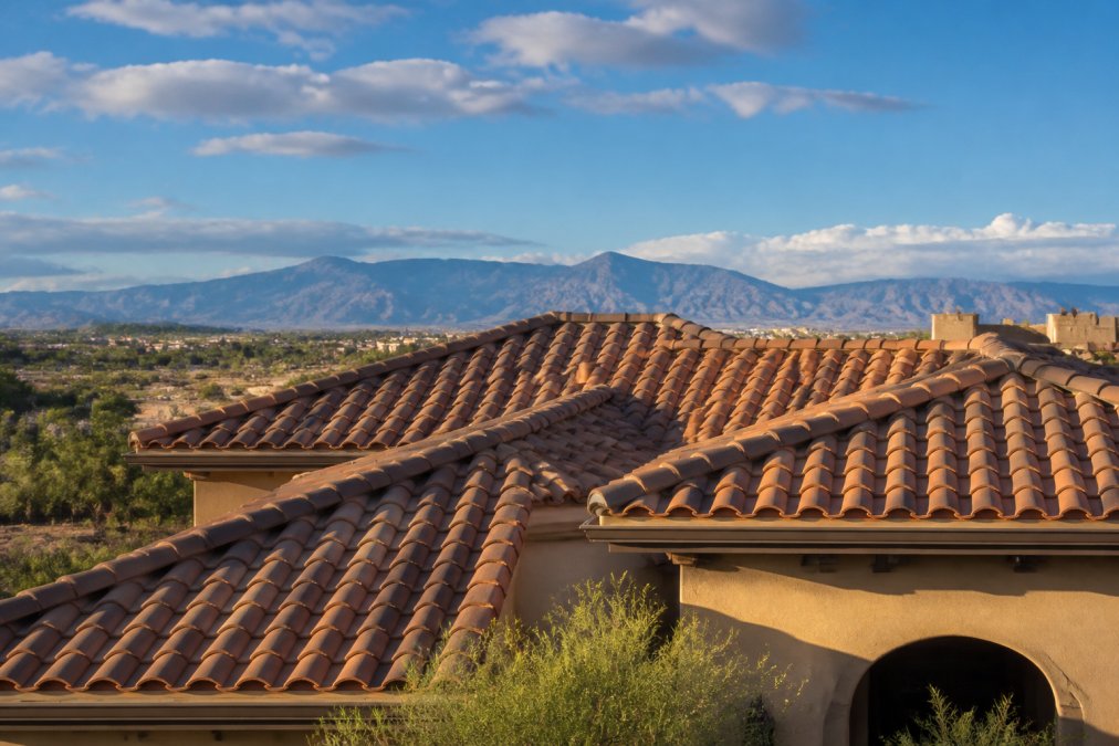 Traditional clay tile roof on Southwest-style home with warm earth-toned tiles catching afternoon desert light, showing varied texture and color variation across curved tiles with distant desert mountains visible