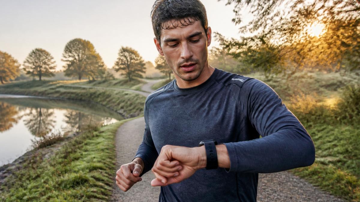 A runner checking their GPS watch mid-run on a scenic park trail, morning light, focused expression