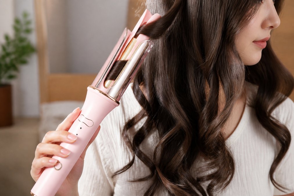 Close-up of a rotating curling wand creating bouncy curls on long hair, showing the barrel wrapping mechanism and resulting voluminous waves
