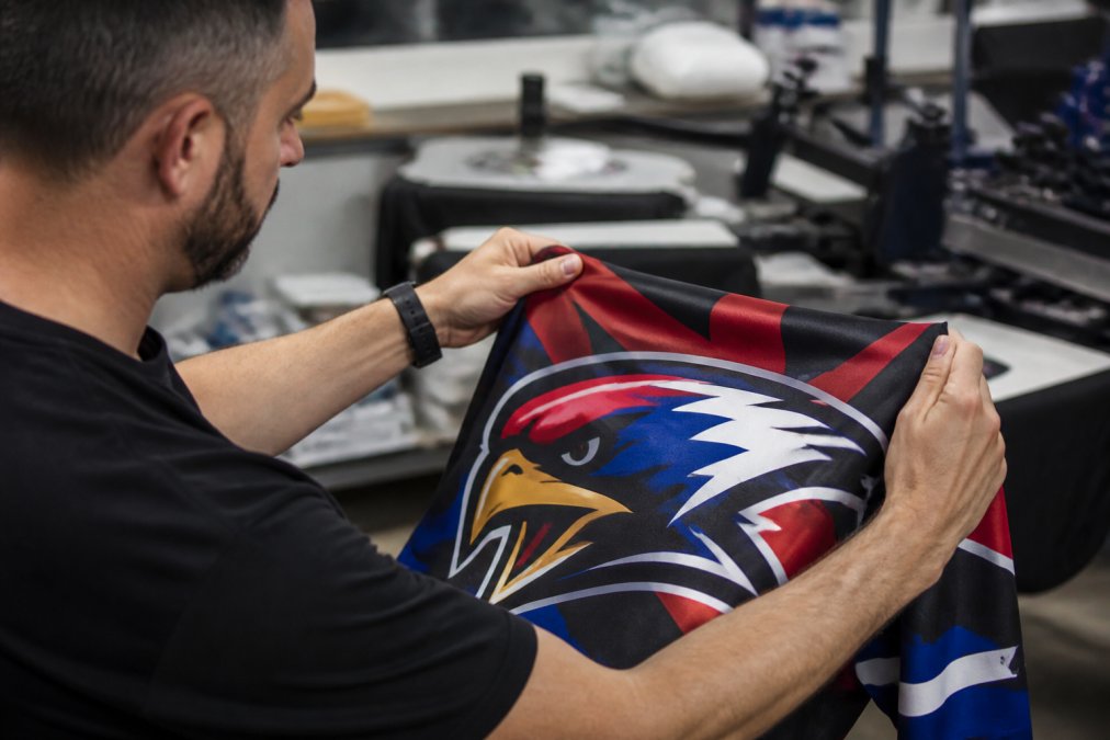 A professional printer's hands inspecting a freshly printed polyester jersey with a vibrant, multicolored team logo under bright workshop lighting