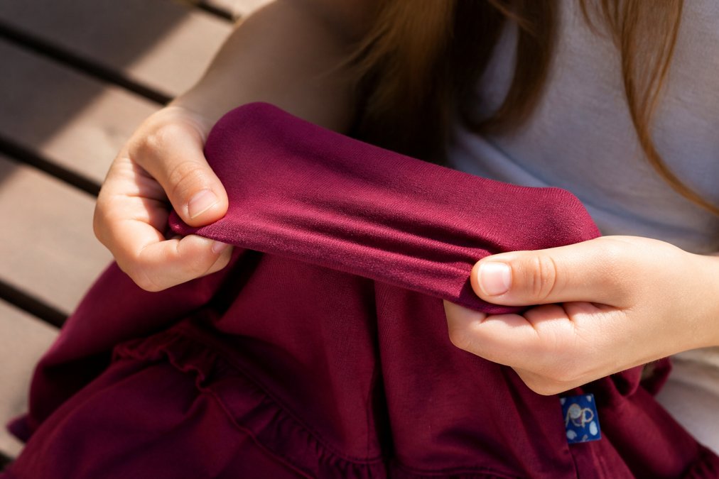 Close-up of a tween girl's hands examining soft bamboo fabric between her fingers, showing the smooth texture and natural drape of sensory-friendly material in natural sunlight