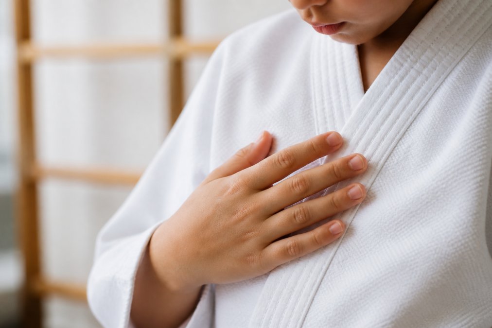 Close-up of a child's hand gently touching the soft fabric weave of a lightweight karate gi, showing the smooth texture and breathable cotton blend under natural daylight