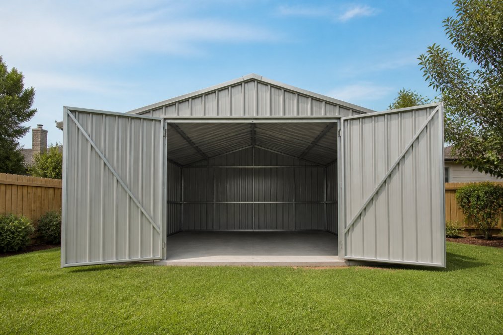 A large galvanized steel storage shed standing in a suburban backyard on a sunny day, double front doors open wide showing the metal frame and interior space, with a neatly trimmed lawn in the foreground and blue sky behind