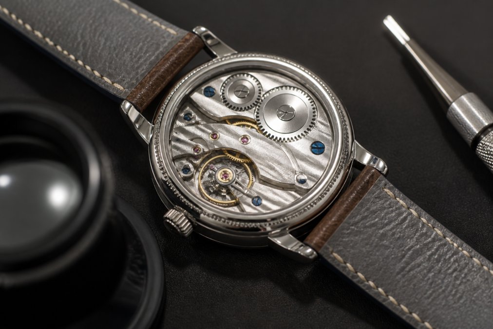 Watch movement visible through exhibition caseback displaying custom caliber with hand-finished bridges and decorated surfaces under magnification lighting