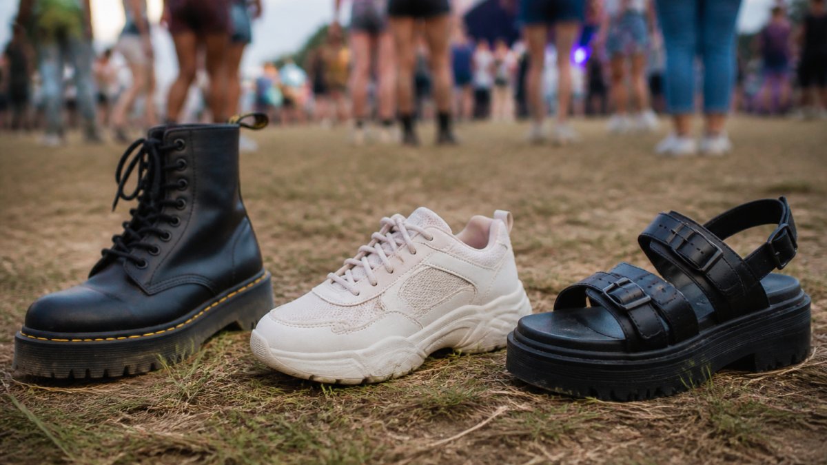 Close-up of three different festival shoe styles, chunky-soled boots, cushioned sneakers, and platform sandals, arranged on a festival ground with grass and dirt visible