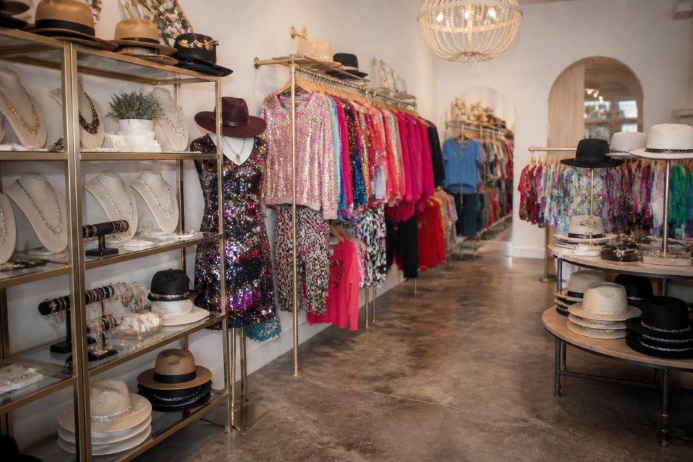 Interior shot of a welcoming boutique storefront displaying vibrant Queen of Sparkles pieces, Stetson hats, and French Kande jewelry on display shelves and colorful racks with warm lighting