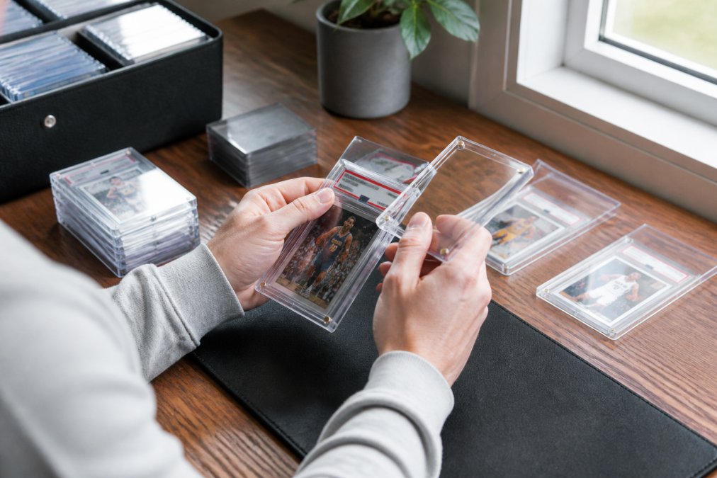Collector placing a PSA card into a magnetic case for slab protection on a desk