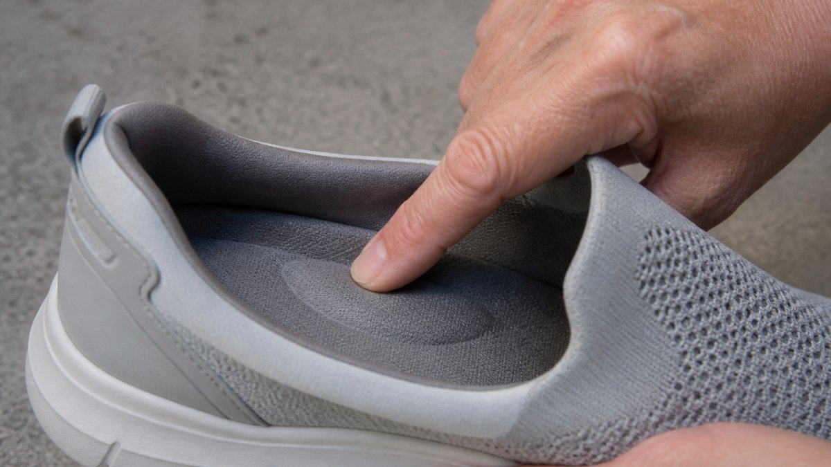 Close-up of a hand touching the cushioned arch support area inside a sneaker, showing the dense midsole structure and anatomical heel counter design