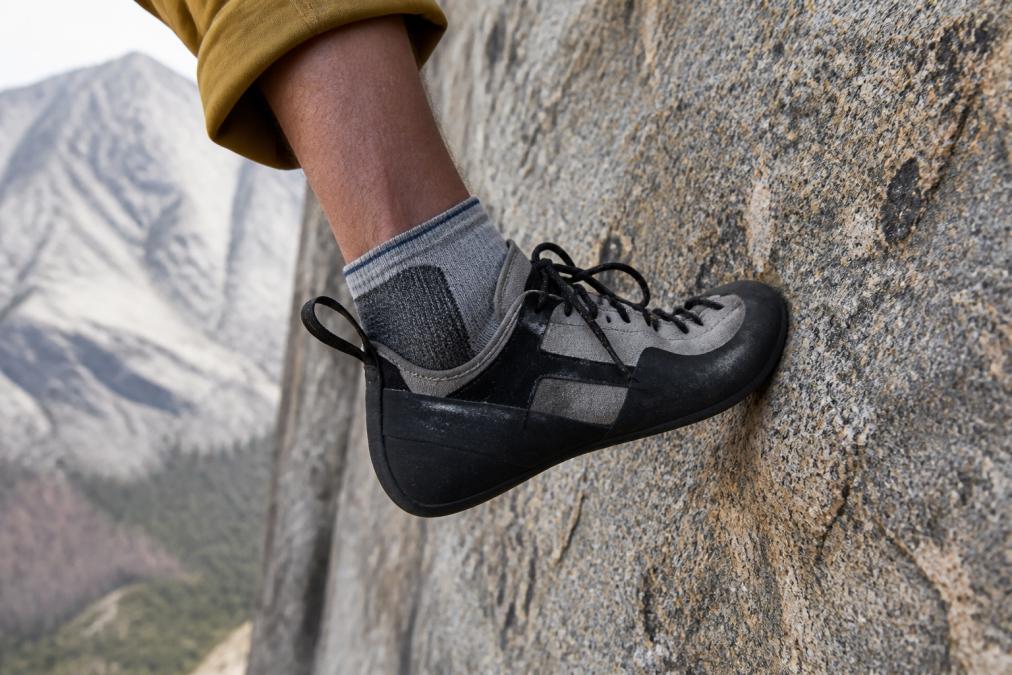 Close-up of climber's foot secured in climbing shoe on granite rock face during multi-pitch ascent, showing sock coverage at heel collar and friction points